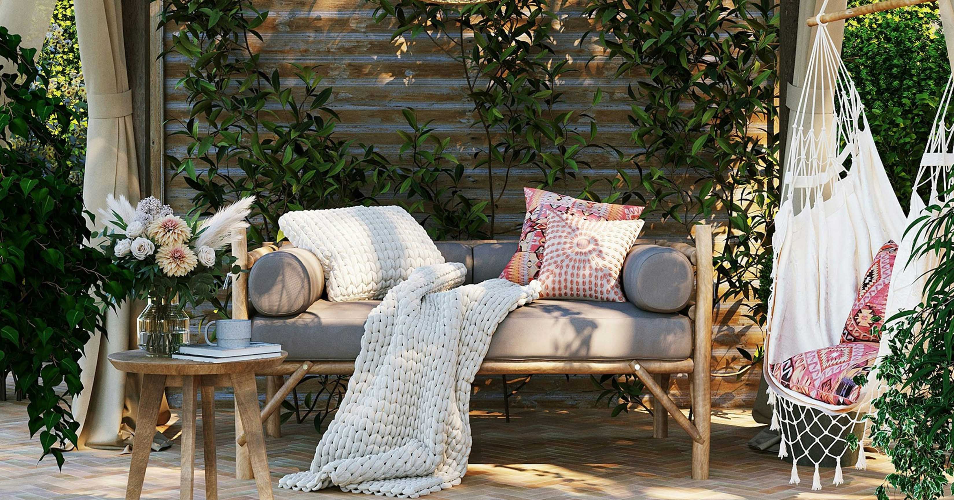 Outdoor setting with a boho style couch with throw cushions and throw rug with a white hammock with red cushions on the right side of the image.